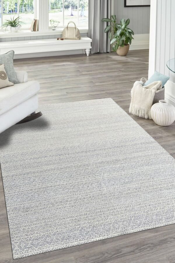 Light silver and white striated rug layered on gray wood floors in a bright, coastal room setting.