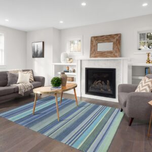 A low-pile rug featuring vertical blue and teal stripes rests on dark wood flooring in a bright living room.