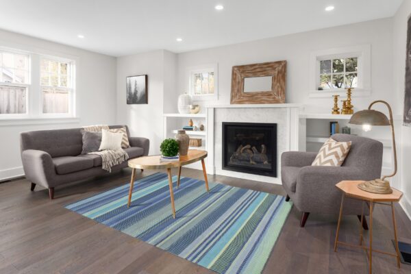 A low-pile rug featuring vertical blue and teal stripes rests on dark wood flooring in a bright living room.