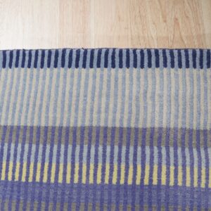 Striped rug in blocks of blue, purple, beige, and yellow rests on light wood flooring.
