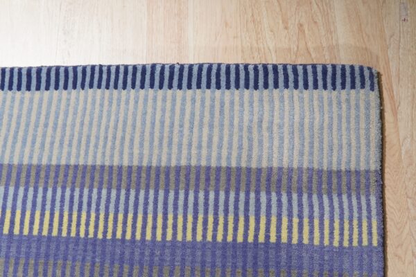Striped rug in blocks of blue, purple, beige, and yellow rests on light wood flooring.