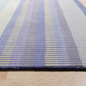 Low-angle view of a striped rug in shades of blue, lavender, and pale yellow on light wood flooring.