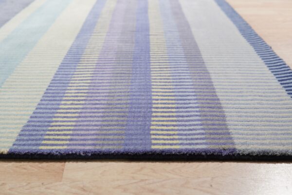 Low-angle view of a striped rug in shades of blue, lavender, and pale yellow on light wood flooring.