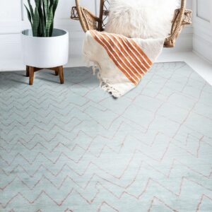 Light blue textured rug with salmon zigzag patterns sits beneath a rattan hanging chair and white planter.