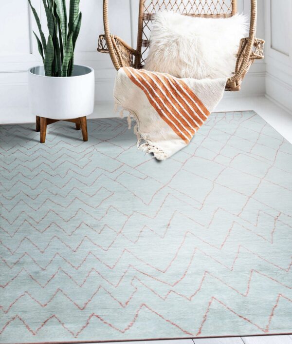 Light blue textured rug with salmon zigzag patterns sits beneath a rattan hanging chair and white planter.