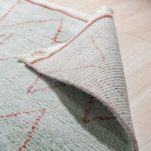 Close-up of a shaggy light blue and red zigzag rug peeled back on light wood flooring.