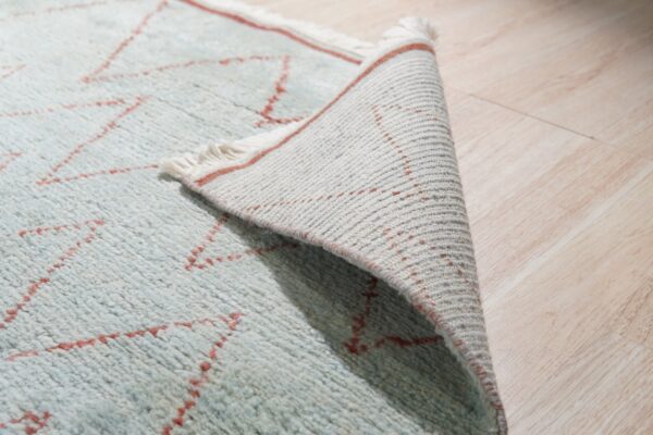 Close-up of a shaggy light blue and red zigzag rug peeled back on light wood flooring.