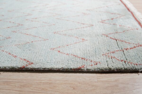 Textured light blue shag rug with thin coral zigzag lines, visible on blonde wood flooring.