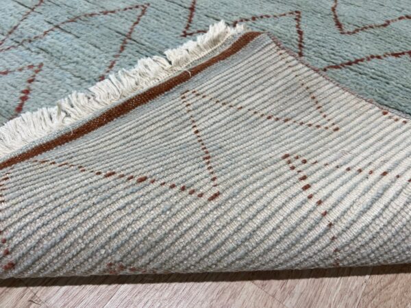 High-pile light blue rug with a reddish pattern is folded over, revealing the ribbed woven backing.