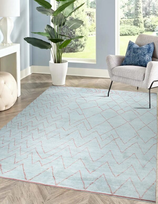 Pale blue geometric rug with coral lines anchors a seating area with a gray chair and potted plant.