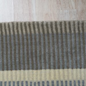 Textured area rug with taupe, blue-gray, and cream striped bands lies on light-colored wood plank flooring.