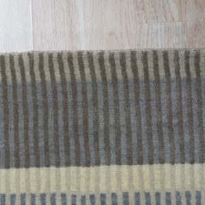 Striped rug with gray, taupe, and cream horizontal color blocks rests on light plank flooring.