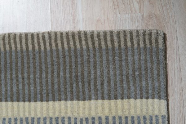 Striped rug with gray, taupe, and cream horizontal color blocks rests on light plank flooring.
