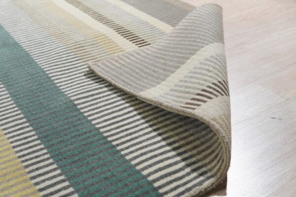 A striped rug in teal, yellow, gray, and cream is rolled up slightly on a light wood floor.