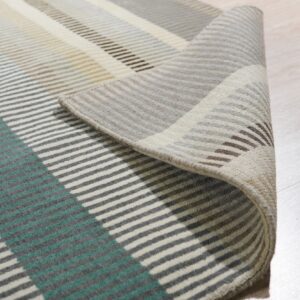 Multicolored striped rug in teal, yellow, and gray, rolled up on light wood flooring.