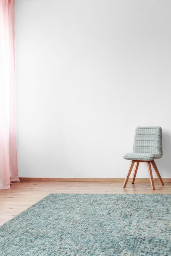 Textured teal rug on light wood floors beside a plaid chair and pink sheer curtains.