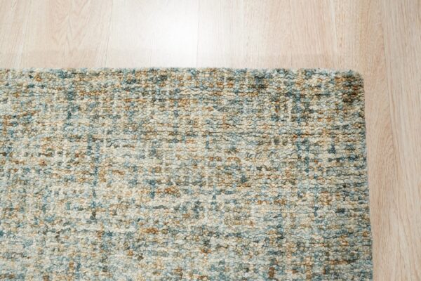 Mottled blue, cream, and tan chunky loop rug texture borders light wooden plank flooring.
