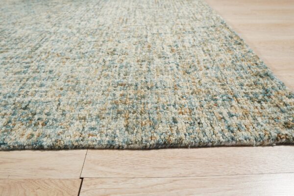 Chunky textured rug in variegated blue, cream, and tan resting on a light wood plank floor.