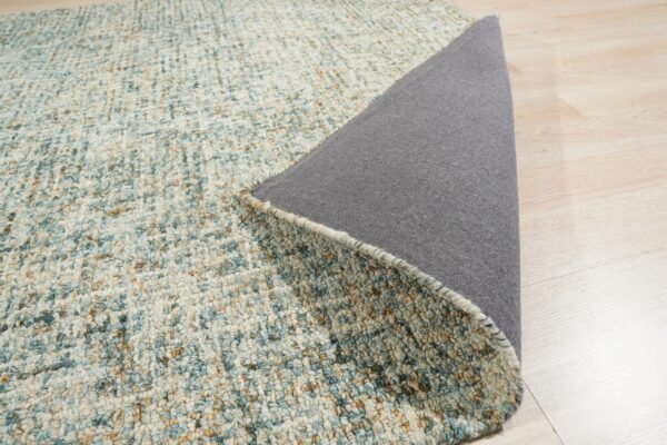 Textured blue and tan speckled rug surface is lifted, exposing the dark gray backing on light wood floors.