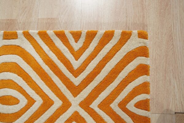 Plush orange and cream rug with a bold geometric pattern visible on light blonde wood flooring.