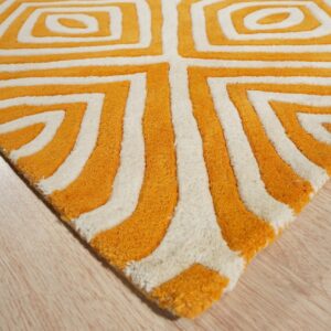 Textured high-pile rug in orange and white with a repeating geometric pattern rests on light wood plank flooring.