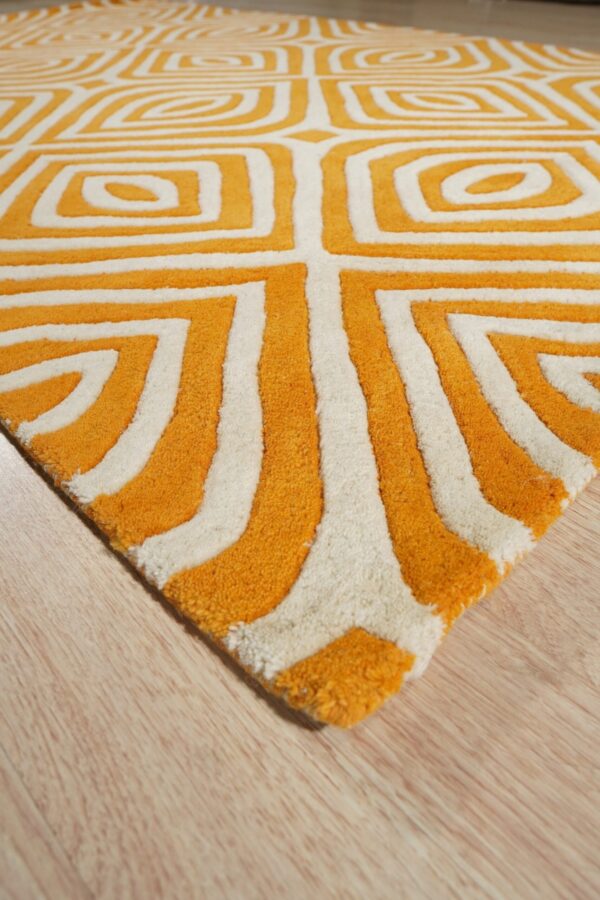 Textured high-pile rug in orange and white with a repeating geometric pattern rests on light wood plank flooring.
