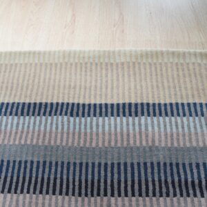 Multicolor striped rug with horizontal bands of navy, blue, gray, and beige on wood planks.