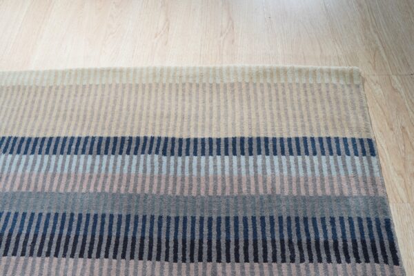 Multicolor striped rug with horizontal bands of navy, blue, gray, and beige on wood planks.