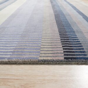 Textured rug with multi-colored vertical stripes in blue, navy, gray, and cream, lying on light wood flooring.