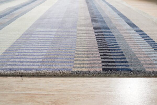 Textured rug with multi-colored vertical stripes in blue, navy, gray, and cream, lying on light wood flooring.