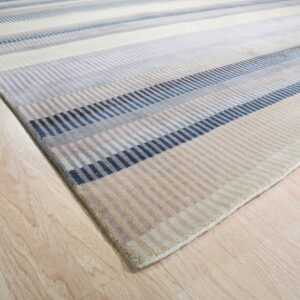Striped rug with segmented blocks of navy, blue, gray, and beige on light wood flooring.