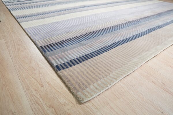 Striped rug with segmented blocks of navy, blue, gray, and beige on light wood flooring.