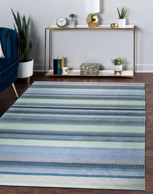Striped blue, gray, and pale green rug on a dark wood floor beside a console table and velvet chair.