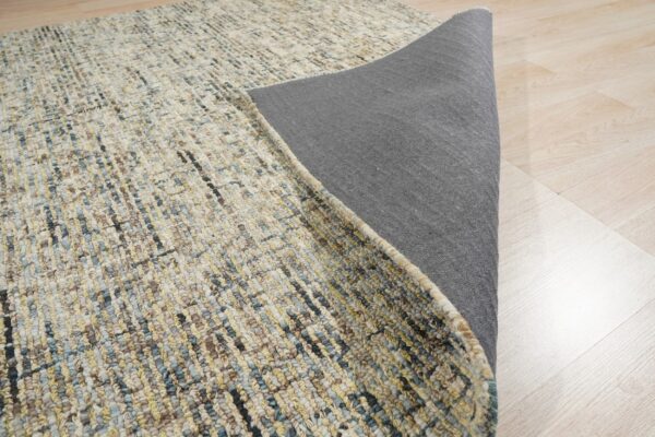 Multi-colored textured rug in blue, yellow, and beige is partially folded, showing a dark gray backing on light wood.