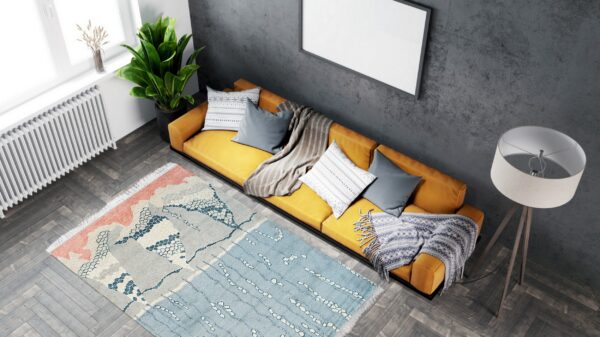 Abstract coral, gray, and blue rug placed on dark wood floors near a mustard yellow sofa.