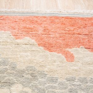 Close-up of a high-pile rug with abstract coral, cream, and gray shapes, resting on light wood flooring.