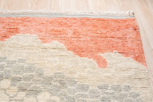 Close-up of a high-pile rug with abstract coral, cream, and gray shapes, resting on light wood flooring.