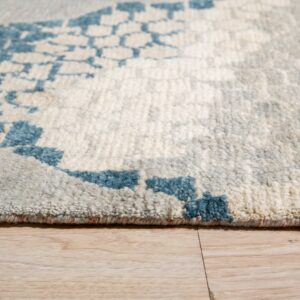 A cream and gray shag rug featuring a bright blue abstract pattern lies on light wood planks.