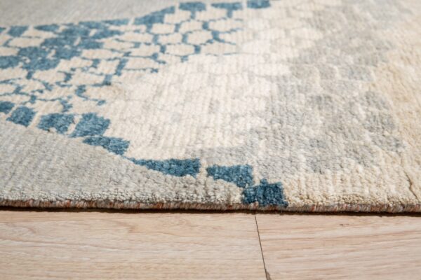 A cream and gray shag rug featuring a bright blue abstract pattern lies on light wood planks.