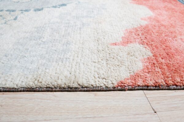 Textured rug corner with white, coral, and blue abstract patterns on light wood plank flooring.