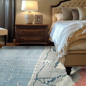 A modern blue and gray abstract rug lays on hardwood floors next to a dark nightstand and upholstered bed.