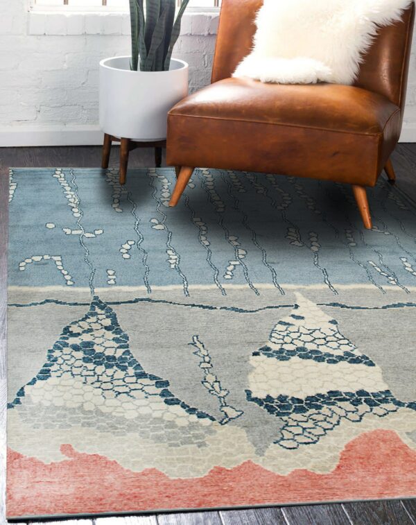 Abstract blue and gray rug with mountain patterns and a coral border under a brown leather chair.