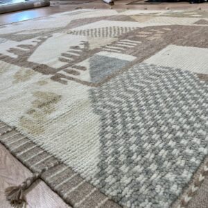 Close-up of a shaggy rug featuring abstract cream, taupe, and gray geometric blocks on wood flooring.