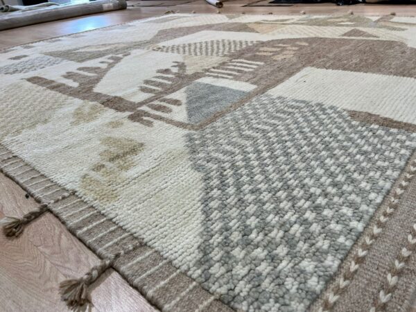 Close-up of a shaggy rug featuring abstract cream, taupe, and gray geometric blocks on wood flooring.