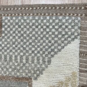 Textured white, gray, and brown checkered rug showing a woven border and tassels on wood floor.