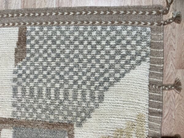 Textured white, gray, and brown checkered rug showing a woven border and tassels on wood floor.