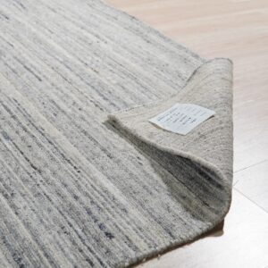 Textured gray and ivory striped rug partially rolled up on light wood plank flooring.