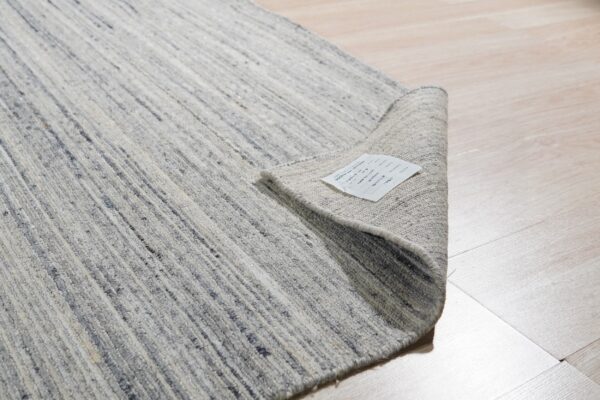 Textured gray and ivory striped rug partially rolled up on light wood plank flooring.