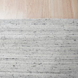 Close-up of a white and gray speckled looped rug resting on light wood flooring.
