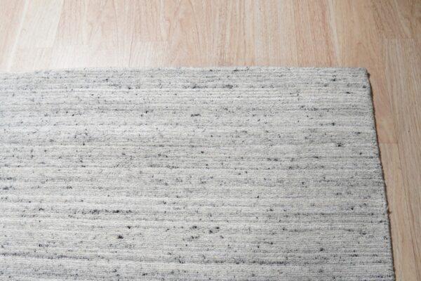 Close-up of a white and gray speckled looped rug resting on light wood flooring.